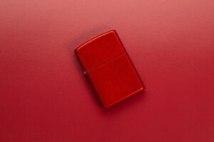 Lifestyle image of Metallic Red Windproof Lighter laying on a red surface
