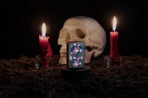 Lifestyle image of Flamingo Skull Design Black Matte Windproof Lighter with a skull and candles in the background.