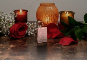 Lifestyle image of Heart Design High Polish Rose Gold Windproof Lighter standing on a table with lit candles and red roses.