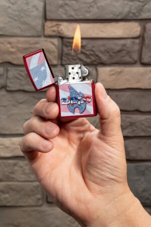 Lifestyle image of Zippo Flag Design Candy Apple Red Windproof Lighter lit in hand.