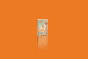 Glamour shot of Zippo Flower Power Design High Polish Brass Windproof Lighter standing in an orange scene.