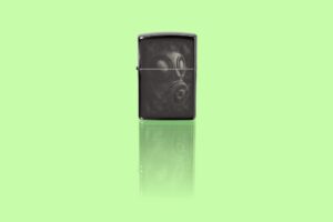Glamour shot of Zippo Gas Mask Design High Polish Black Pocket Lighter standing in a green scene.