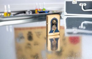 Lifestyle shot of Zippo Tiger Tattoo Design Tumbled Brass Windproof Lighter standing in on a reflective table with tattoo equipment.