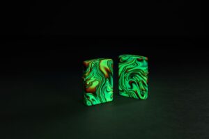 Glamour shot of two Zippo Colorful Swirl Design Glow in the Dark 540 Color Windproof Lighters, one showing the front and the other showing the back, glowing in the dark.